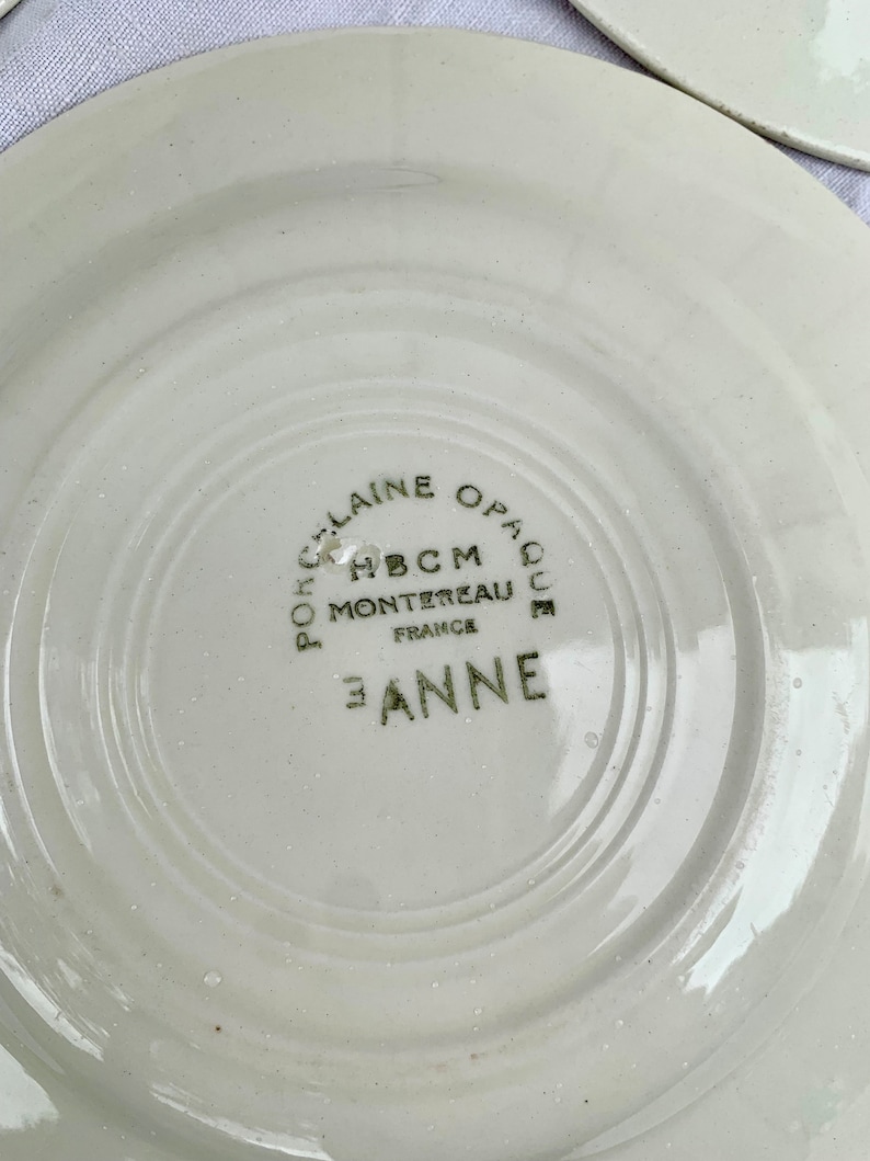 May include: White ceramic plate with a green inscription that reads "Porcelaine Opaque HBCM Montereau France E. Anne".