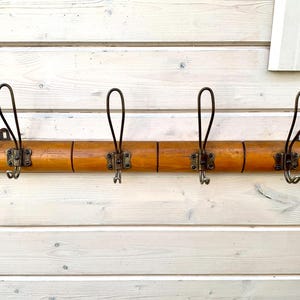 May include: A wooden coat rack with four hooks. The rack is made of light brown wood and has a natural finish. The hooks are made of metal and are black.