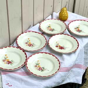 May include: Set of six white ceramic plates with a scalloped edge and a red rim. Each plate features a floral design with red, yellow, and green flowers.