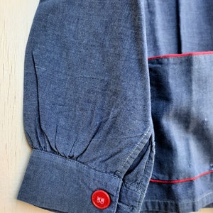 Puede incluir: Una camisa vaquera azul con ribete rojo y un bot&oacute;n rojo en el pu&ntilde;o.
