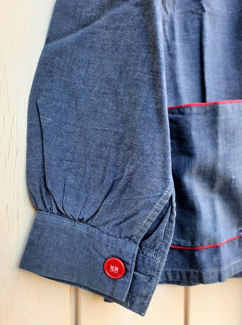 Puede incluir: Una camisa vaquera azul con ribete rojo y un bot&oacute;n rojo en el pu&ntilde;o.