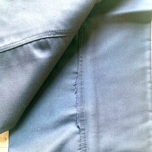 May include: Close-up of a dark blue fabric with a seam running down the center. The fabric is folded over, revealing the underside of the fabric.