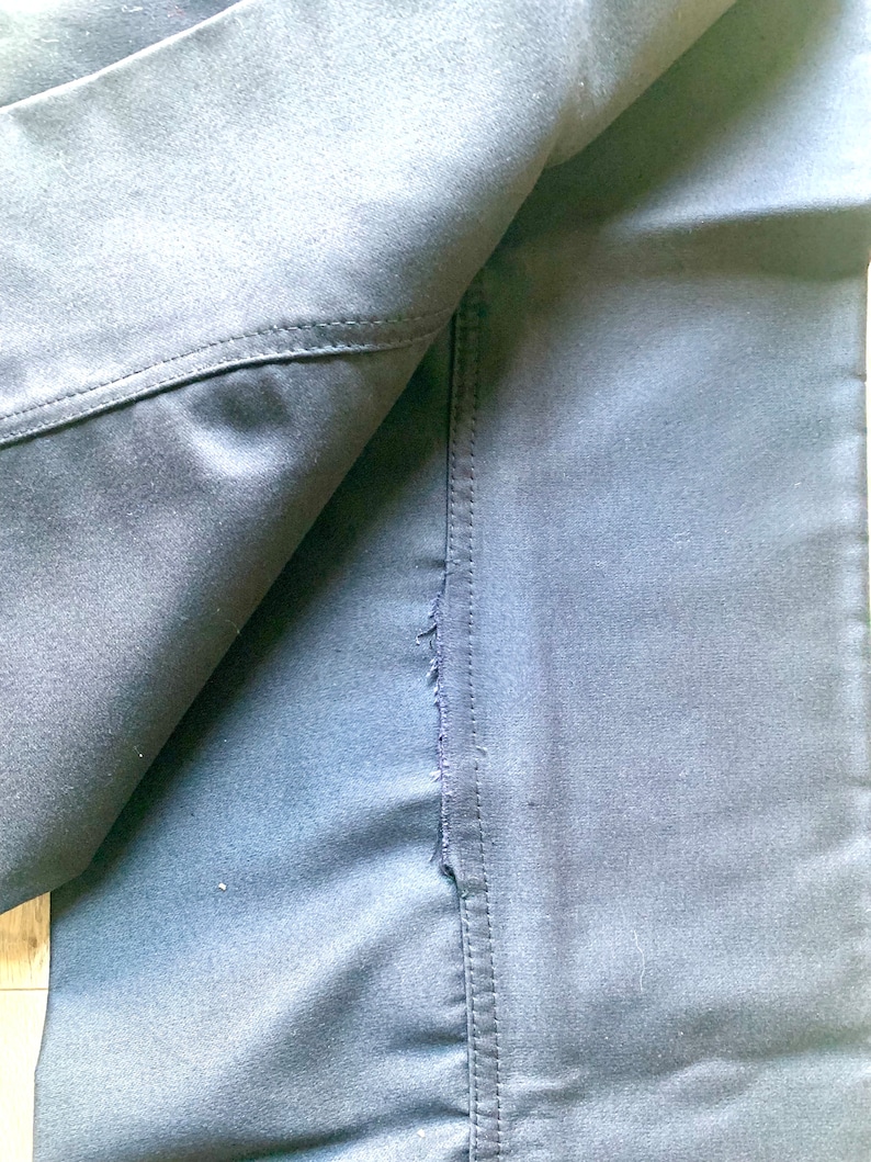 May include: Close-up of a dark blue fabric with a seam running down the center. The fabric is folded over, revealing the underside of the fabric.