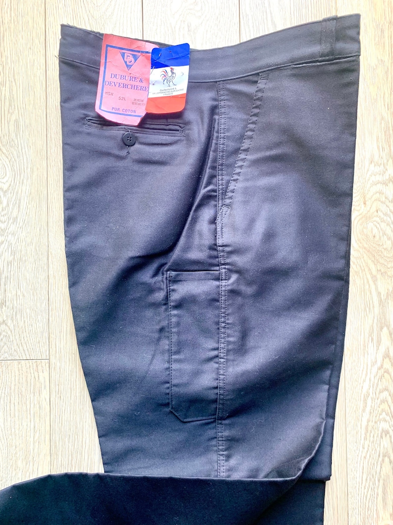 May include: Black pants with a single front pocket and a label that reads "Dubure & Deverchere" with the text "100% Cotton" underneath.