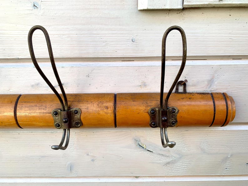 May include: A wooden coat rack with two metal hooks. The rack is made of light brown wood and has a natural finish. The hooks are made of metal and have a dark brown finish.
