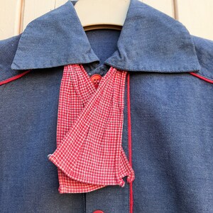 Puede incluir: Una camisa azul marino con una corbata de lazo a cuadros rojos y blancos. La camisa tiene ribetes rojos alrededor del cuello y en la parte delantera.