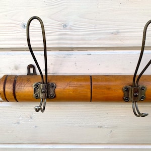 May include: A wooden coat rack with two brass hooks. The rack is made of light brown wood with a dark brown stain. The hooks are attached to the rack with metal brackets.