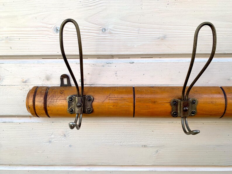 May include: A wooden coat rack with two brass hooks. The rack is made of light brown wood with a dark brown stain. The hooks are attached to the rack with metal brackets.
