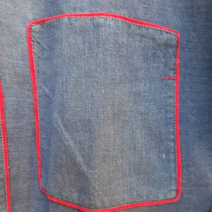 Puede incluir: Una chaqueta vaquera azul con un bolsillo cosido en rojo.