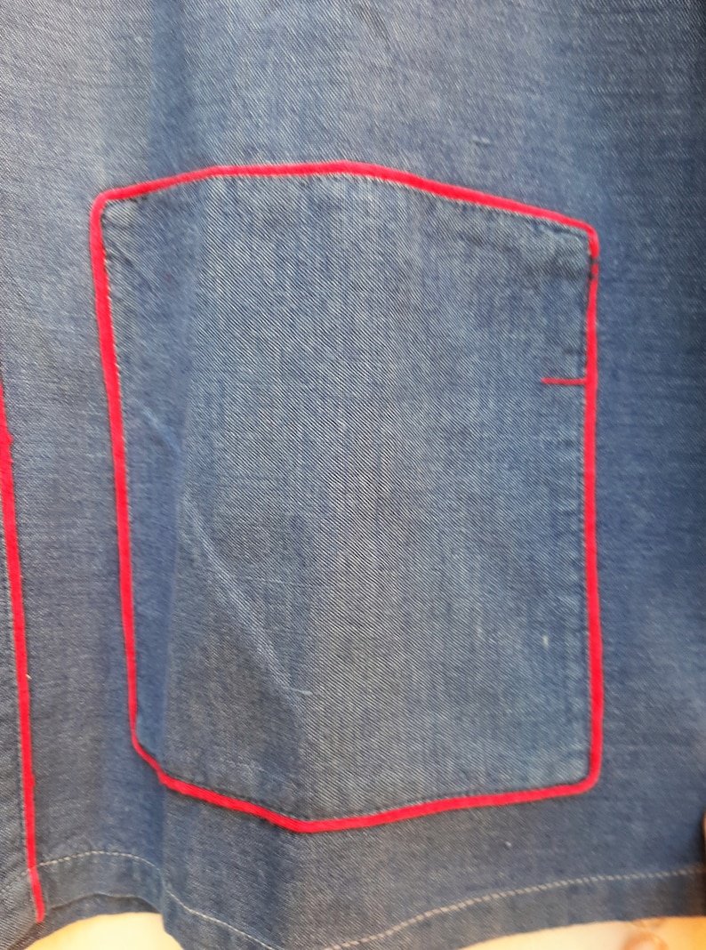 Puede incluir: Una chaqueta vaquera azul con un bolsillo cosido en rojo.