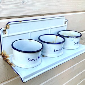 May include: White enamel shelf with three white enamel cups. The cups have blue rims and blue lettering that reads "Savon Mira" and "Cristal".