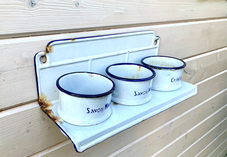May include: White enamel shelf with three white enamel cups. The cups have blue rims and blue lettering that reads "Savon Mira" and "Cristal".