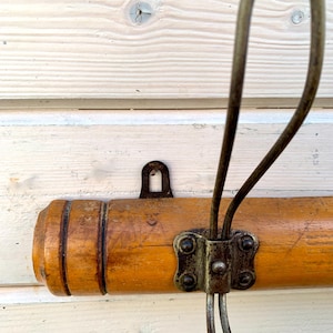 May include: A wooden coat rack with a metal hook. The rack is brown and has a natural wood finish. The hook is silver and has a simple design.