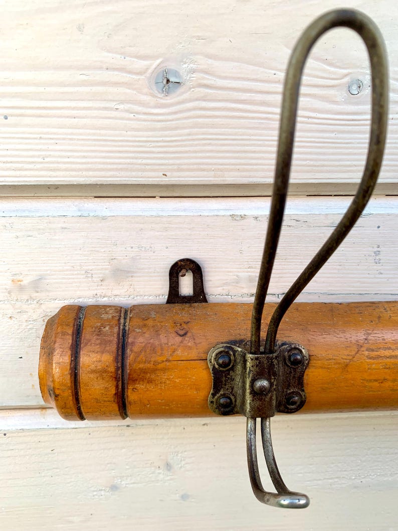May include: A wooden coat rack with a metal hook. The rack is brown and has a natural wood finish. The hook is silver and has a simple design.