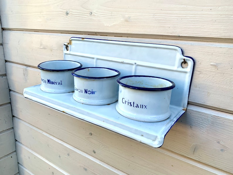 May include: White enamel shelf with three white enamel containers with blue rims and blue lettering. The containers are labeled "Sel Mineral", "Savon Noir", and "Cristaux".