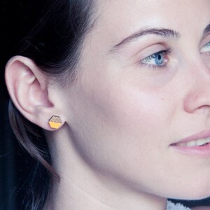 May include: A woman with long dark hair wearing a small yellow and black geometric earring.