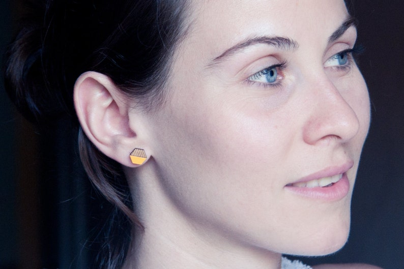 May include: A woman with long dark hair wearing a small yellow and black geometric earring.