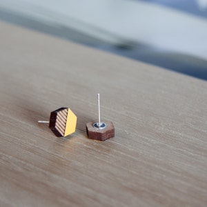 May include: A pair of hexagonal wooden earrings with a yellow and brown striped design. The earrings are on a light brown wooden surface.