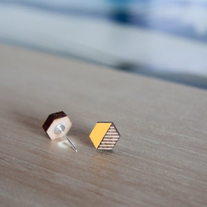 May include: A pair of wooden earrings with a geometric hexagon shape. One earring is brown wood, the other is brown wood with a yellow accent.