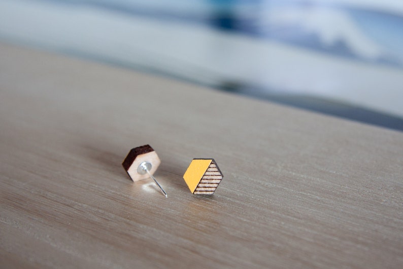 May include: A pair of wooden earrings with a geometric hexagon shape. One earring is brown wood, the other is brown wood with a yellow accent.