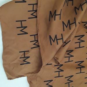 May include: Brown fabric with a repeating pattern of the letters "MH" in black.