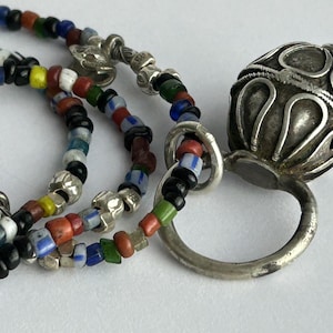 May include: Close-up of a necklace with colorful glass beads and silver accents. The necklace features a variety of small, round beads in red, blue, green, yellow, and black. A silver pendant with an ornate design is also visible.