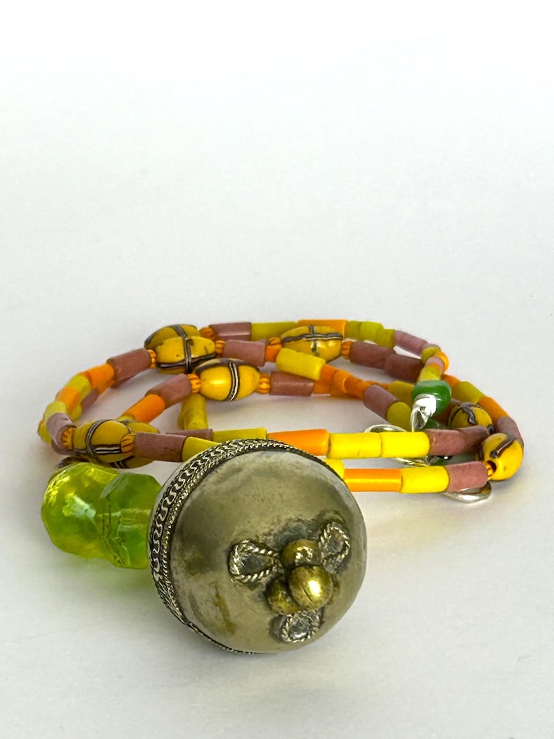 May include: A silver-colored metal bottle stopper with a decorative floral design and a green glass stopper. A necklace with yellow, orange, and pink beads is also in the image. The beads are strung together with a yellow cord.