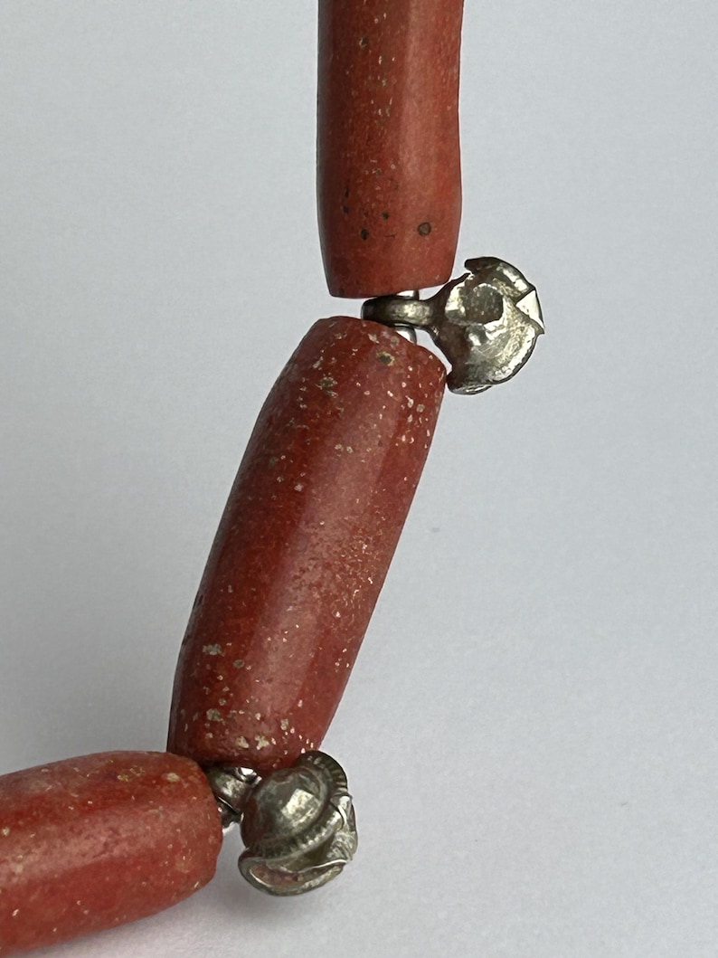 Pode incluir: Close-up de um colar com contas cil&iacute;ndricas castanho-avermelhadas. As contas s&atilde;o conectadas por fechos prateados ornamentados. O colar tem uma est&eacute;tica r&uacute;stica e terrosa.