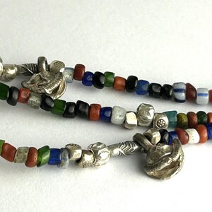 May include: Close-up of three strands of colorful beaded necklaces. The beads are in various colors, including red, green, blue, and white. Silver-toned metal charms and clasps are interspersed throughout the strands.