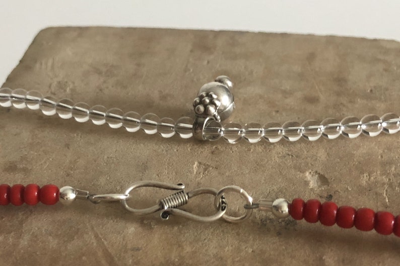May include: Two necklaces with silver clasps. One necklace is made of clear beads and the other is made of red beads.