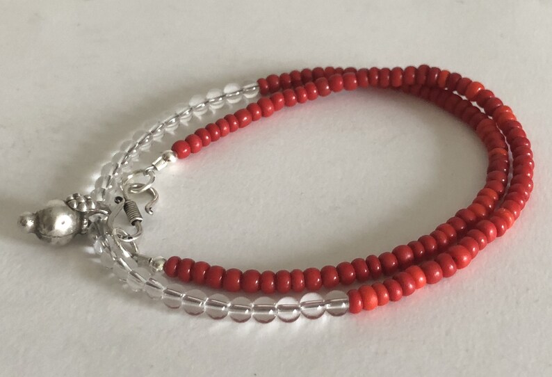 May include: A red and clear beaded bracelet with a silver charm. The bracelet is made of small, round beads and has a spring clasp.