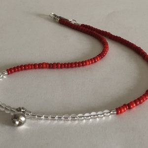 May include: A red and clear beaded necklace with a silver charm. The necklace is made of small, round beads and has a simple design.