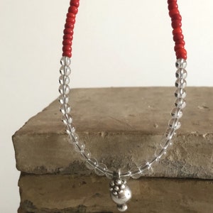 May include: A necklace made with clear and red beads with a silver charm at the end.
