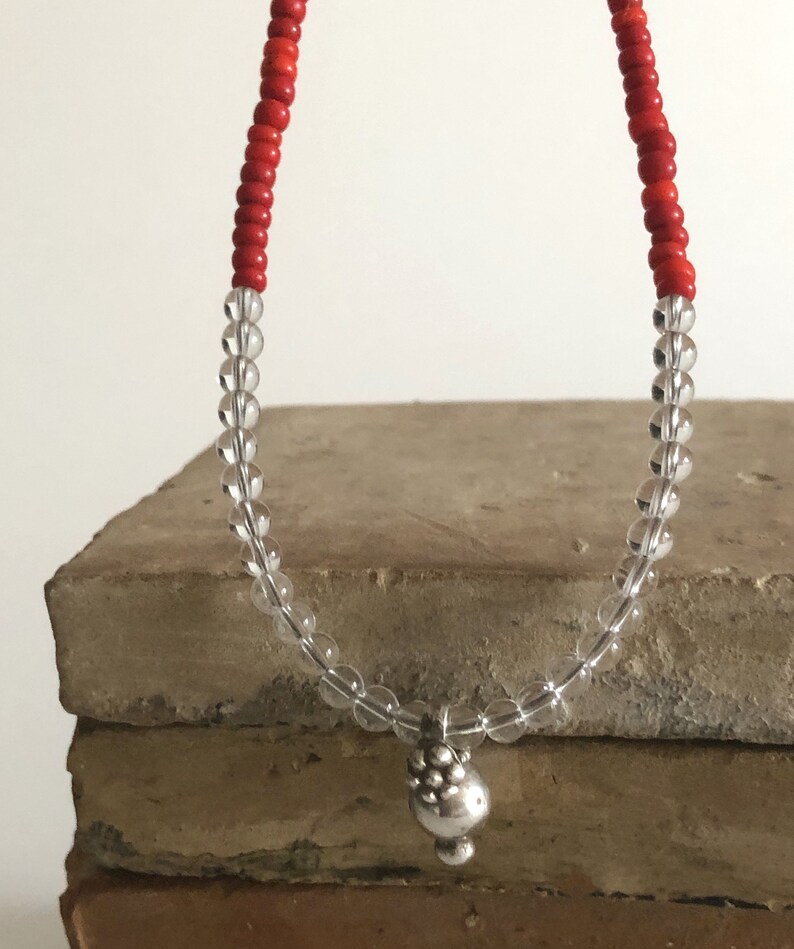 May include: A necklace made with clear and red beads with a silver charm at the end.