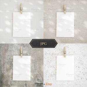 May include: Four vertical white rectangular cards hanging from a thin horizontal string by wooden clothespins. Each card is displayed against a different textured background, including smooth light gray, beige, dark gray stone, and white stone.