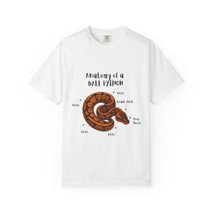 May include: White t-shirt with a detailed illustration of a ball python and anatomical labels. The snake is brown and orange, coiled in a circular shape. The text "Anatomy of a Ball Python" is above the snake.