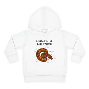 May include: White hooded sweatshirt featuring a detailed illustration of a ball python with labeled anatomical parts. The text "Anatomy of a Ball Python" is printed above the snake graphic. The snake is brown and orange.