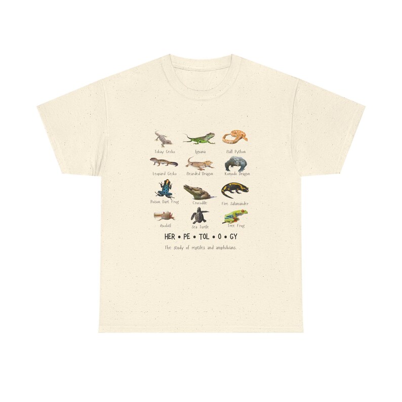 May include: Cream-colored t-shirt featuring a colorful illustration of various reptiles and amphibians, including geckos, iguanas, and frogs. The word "HERPETOLOGY" is printed below the illustrations, along with the phrase "The study of reptiles and amphibians."