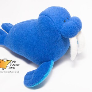 May include: A blue plush toy walrus with white tusks. The walrus has a blue and turquoise flipper and is lying on a white surface.