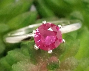May include: A silver ring with a bright pink gemstone set in a four-prong setting.