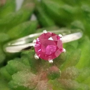 Puede incluir: Un anillo de plata con una piedra preciosa rosa brillante engastada en un engaste de cuatro garras.