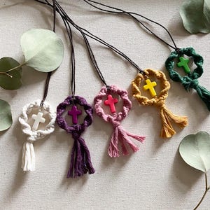 Może przedstawiać: Pięć ręcznie robionych naszyjników z makramą z zawieszką w kształcie krzyża. Każdy naszyjnik ma inny kolor makramą i inny kolor zawieszki w kształcie krzyża. Kolory obejmują biały, fioletowy, różowy, żółty i zielony.