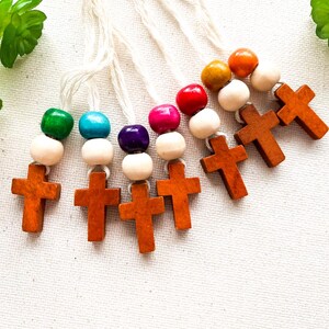 May include: A set of seven wooden cross charms with colourful beads and white string. The crosses are brown and the beads are red, orange, yellow, green, blue, purple and pink.