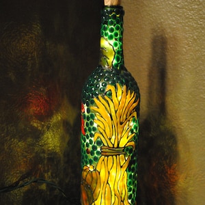 May include: A decorative wine bottle with a cork stopper, featuring a green, textured exterior. The bottle is illuminated from within, showcasing a yellow wheat sheaf design and a pumpkin. The bottle is a unique home decor item.