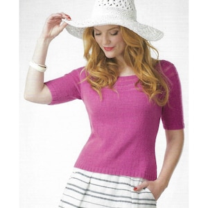 Può includere: Un maglione a maniche corte color magenta brillante con scollo rotondo e orlo a coste, abbinato a un cappello da sole bianco con un delicato motivo traforato e una gonna bianca decorata con strisce orizzontali grigie.