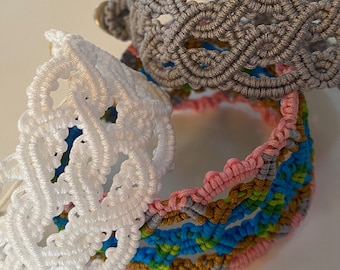 Könnte beinhalten: Eine Sammlung von Makramee-Armbändern in verschiedenen Farben. Die Armbänder umfassen Weiß, Grau und ein mehrfarbiges Armband mit rosa, blauen und goldenen Akzenten. Die Makramee-Designs weisen komplizierte Webmuster auf und zeigen die handwerkliche Verarbeitung.