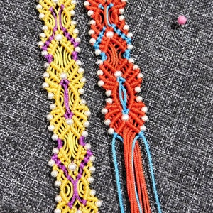 May include: Two macrame bracelets. One is yellow, purple, and silver. The other is red, blue, and silver. Both have intricate woven patterns and dangling threads. The bracelets are handmade and colorful.