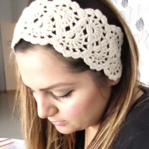 May include: A white crocheted headband with a delicate floral design. The headband is worn by a person with long brown hair.