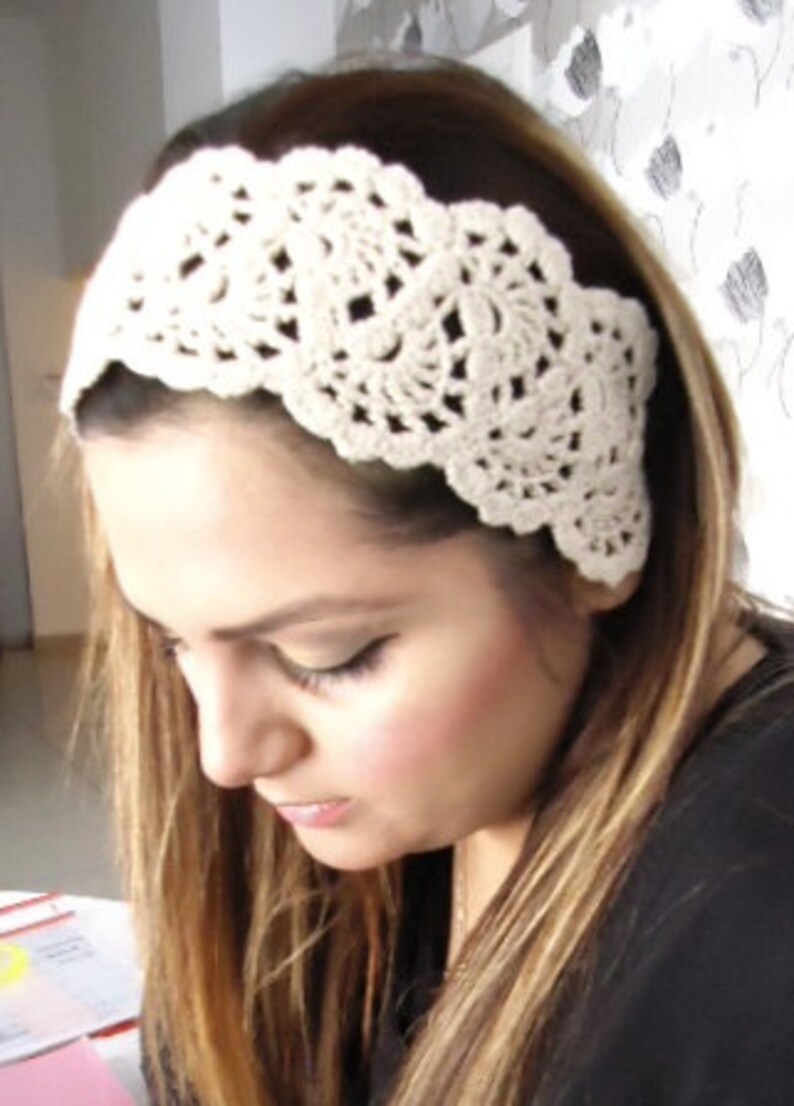 May include: A white crocheted headband with a delicate floral design. The headband is worn by a person with long brown hair.