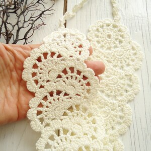 May include: A white crocheted collar necklace with a delicate, lacy design. The necklace is made of fine yarn and has a scalloped edge.